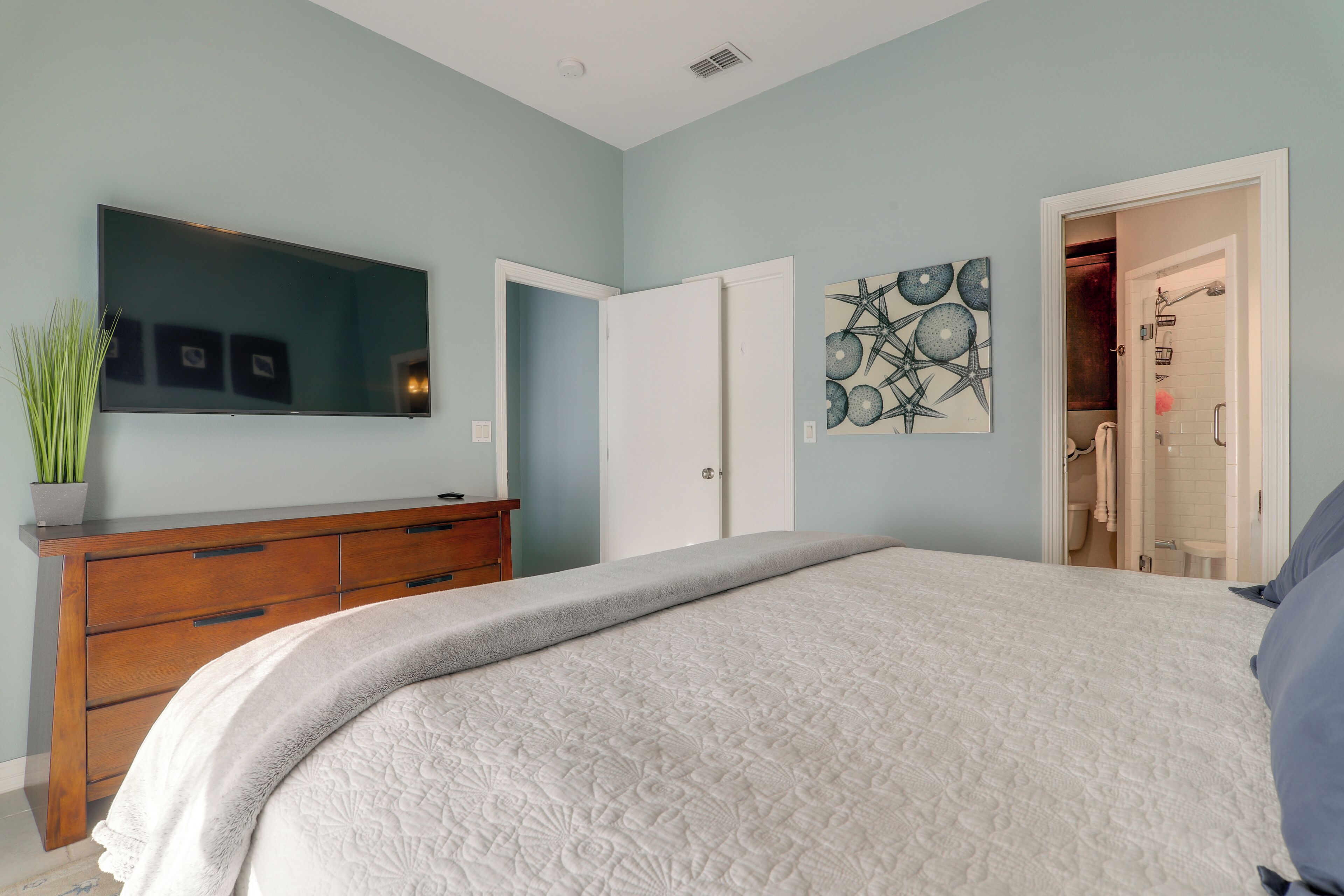 Une chambre à coucher comprenant un lit, une commode, un téléviseur à écran plat et une porte donnant accès à une salle de bain.