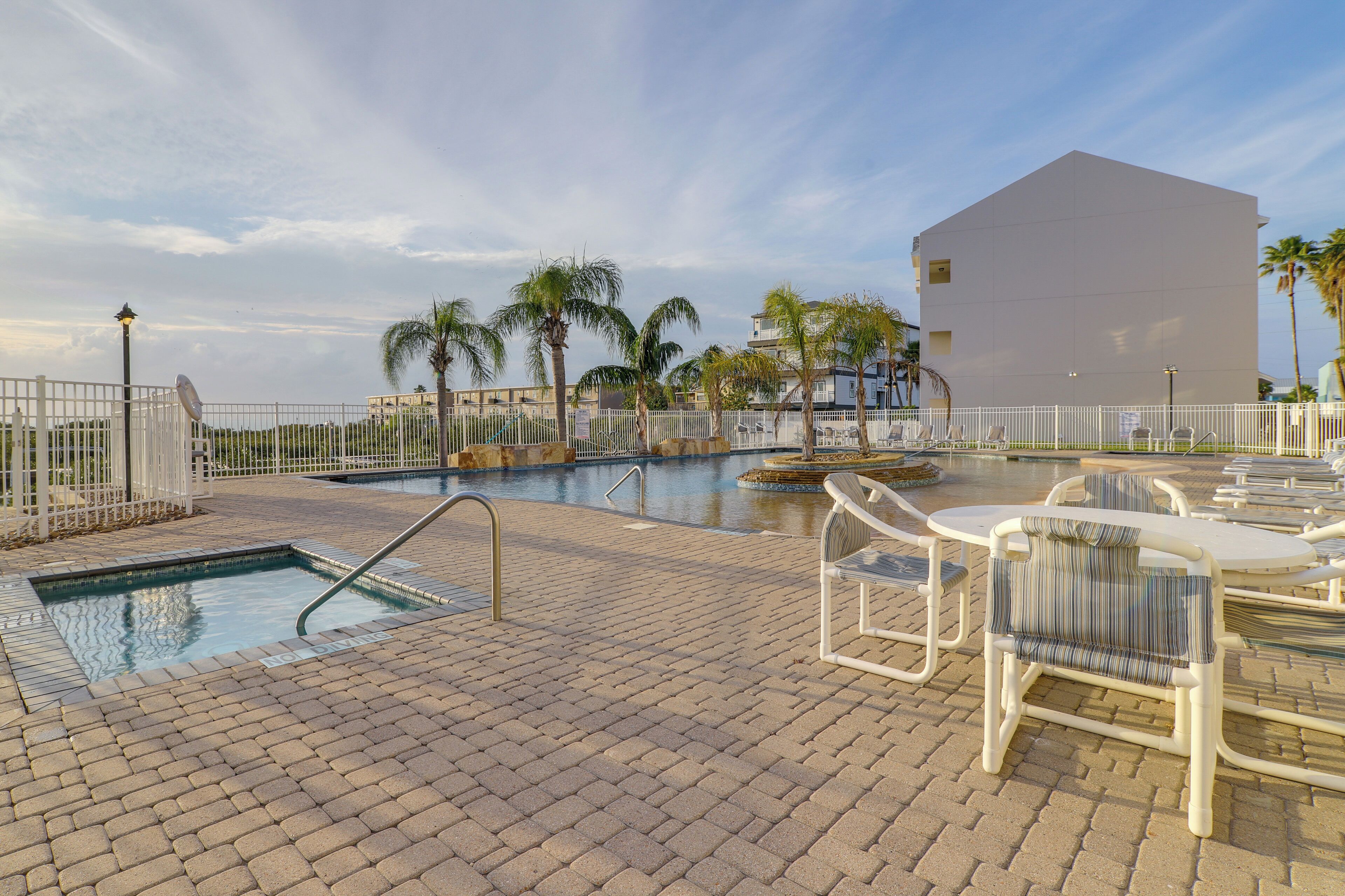 A pool area with a rectangular pool, lounge chairs, and a white building in the background.
