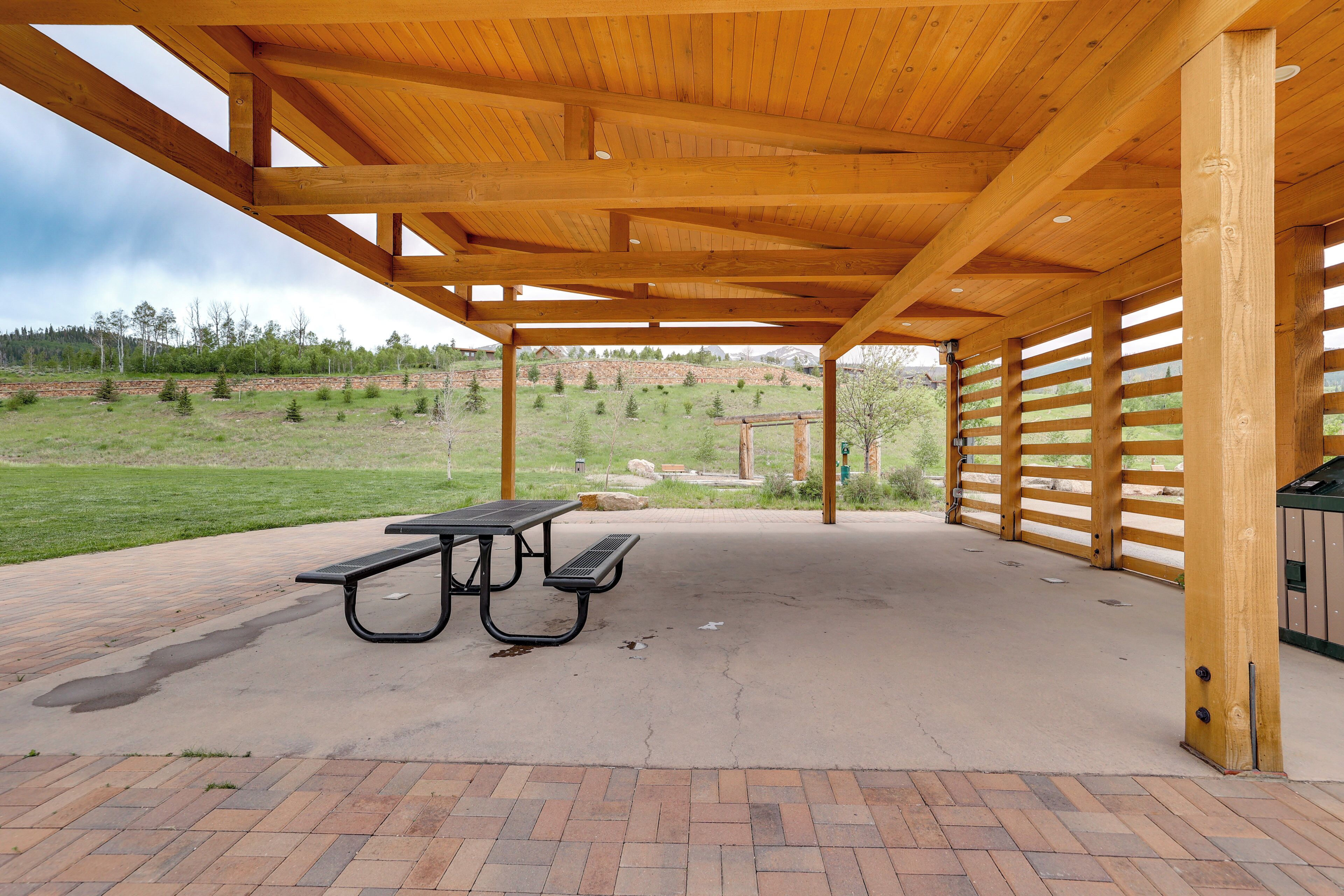 A covered picnic area with a picnic table and benches, surrounded by a brick patio and wooden beams.