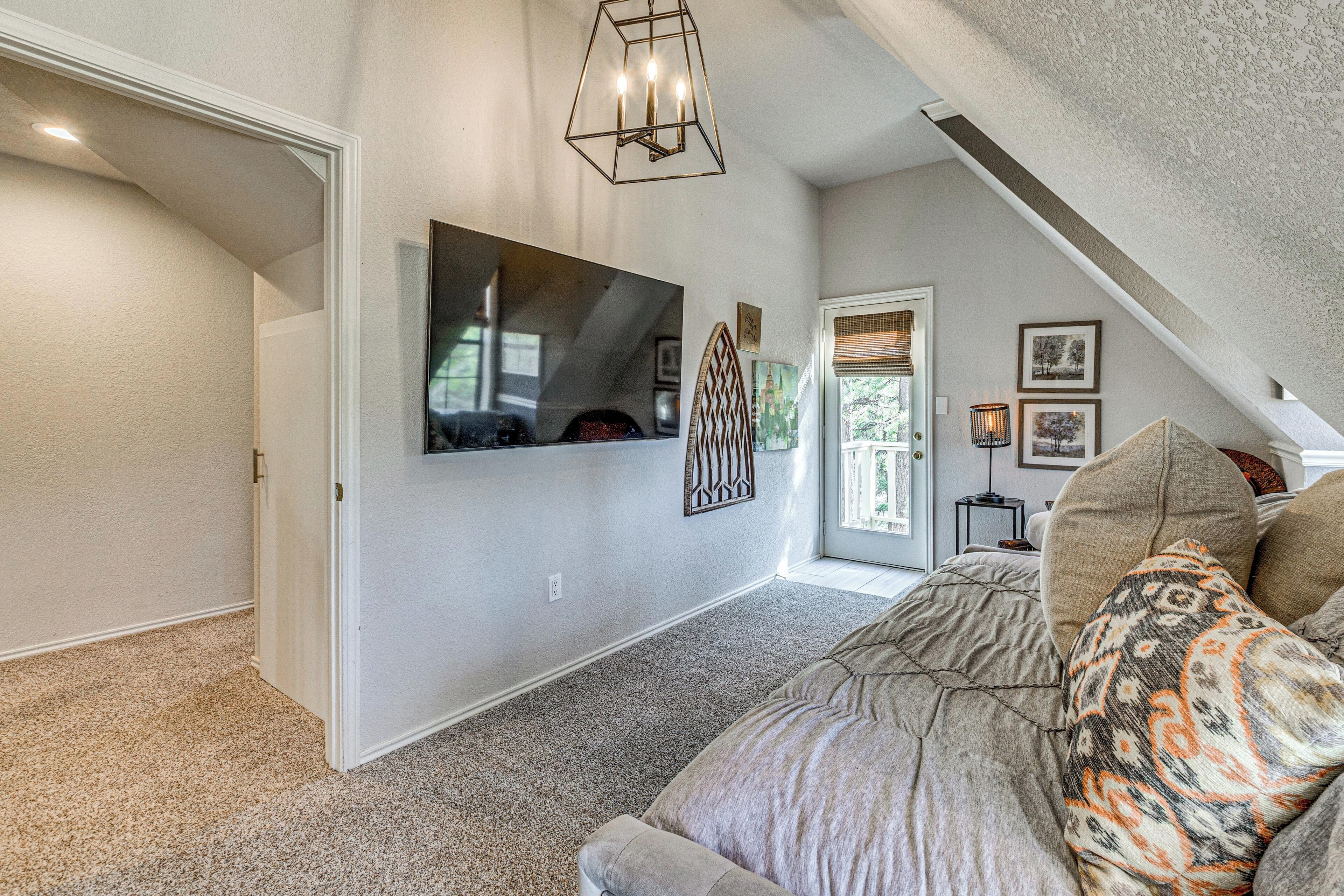 A spacious living area with a large sofa, a flat-screen TV mounted on the wall, and a ceiling light fixture.
