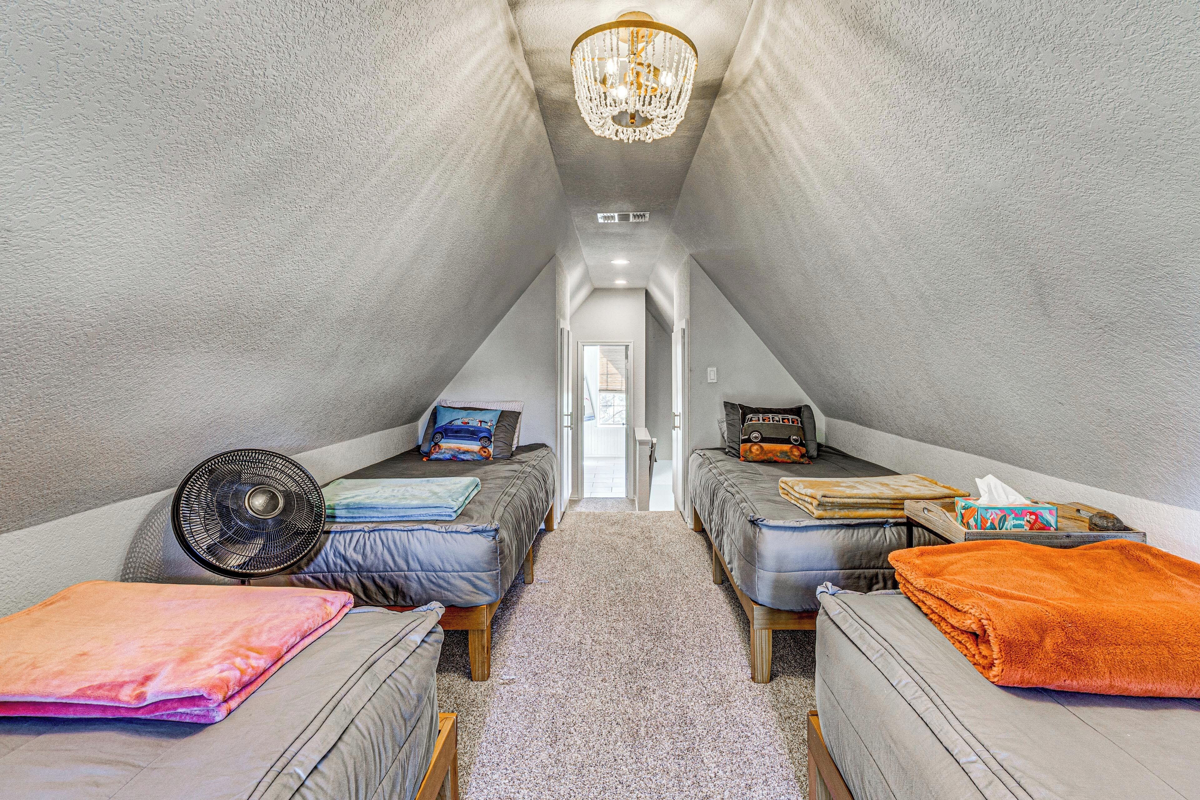 A triangular attic bedroom with two beds, a ceiling fan, and a chandelier.