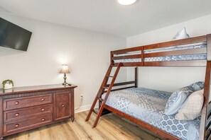 A bunk bed with a ladder, a dresser with drawers, a lamp, and a television on the wall.