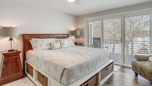 Une chambre dotée d’un grand lit, de deux tables de chevet avec des lampes, d’un ventilateur de plafond et d’une porte-fenêtre coulissante donnant sur un balcon.