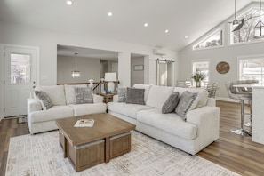 A modern living room with a sectional sofa, a wooden coffee table, and a dining area with a bar. - Hot Tub + Fire Pits: Waterfront Lake Anna Escape! (Louisa)