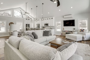 A spacious living room with a large gray sectional sofa, a wooden coffee table, and a TV mounted on the wall. - Hot Tub + Fire Pits: Waterfront Lake Anna Escape! (Louisa)