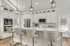 A modern kitchen with white cabinets, stainless steel appliances, and bar stools.