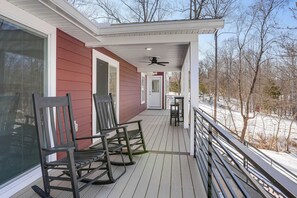 A covered porch with rocking chairs and a table, overlooking a snowy landscape.