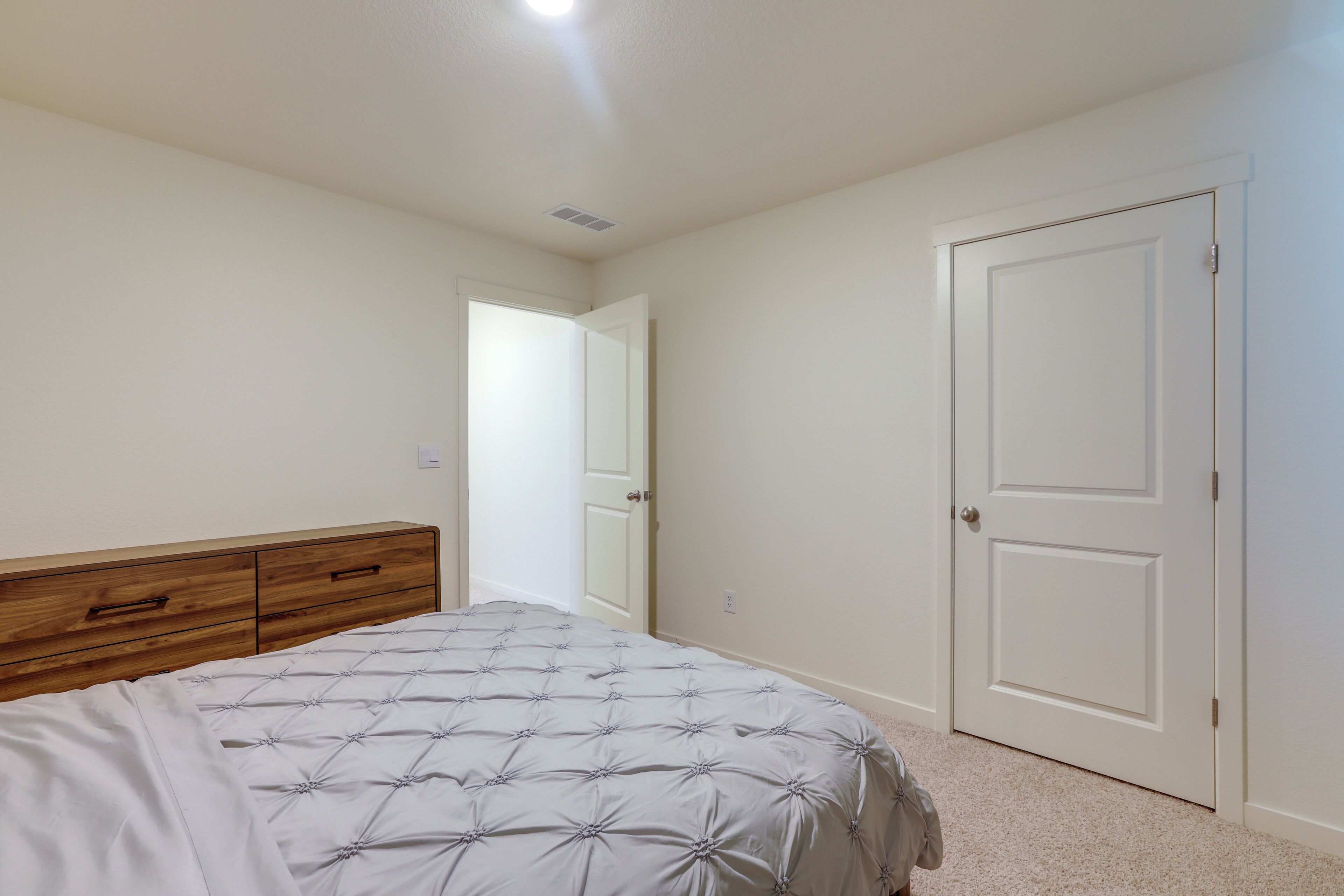 A bedroom with a bed, a wooden dresser, and a white door.