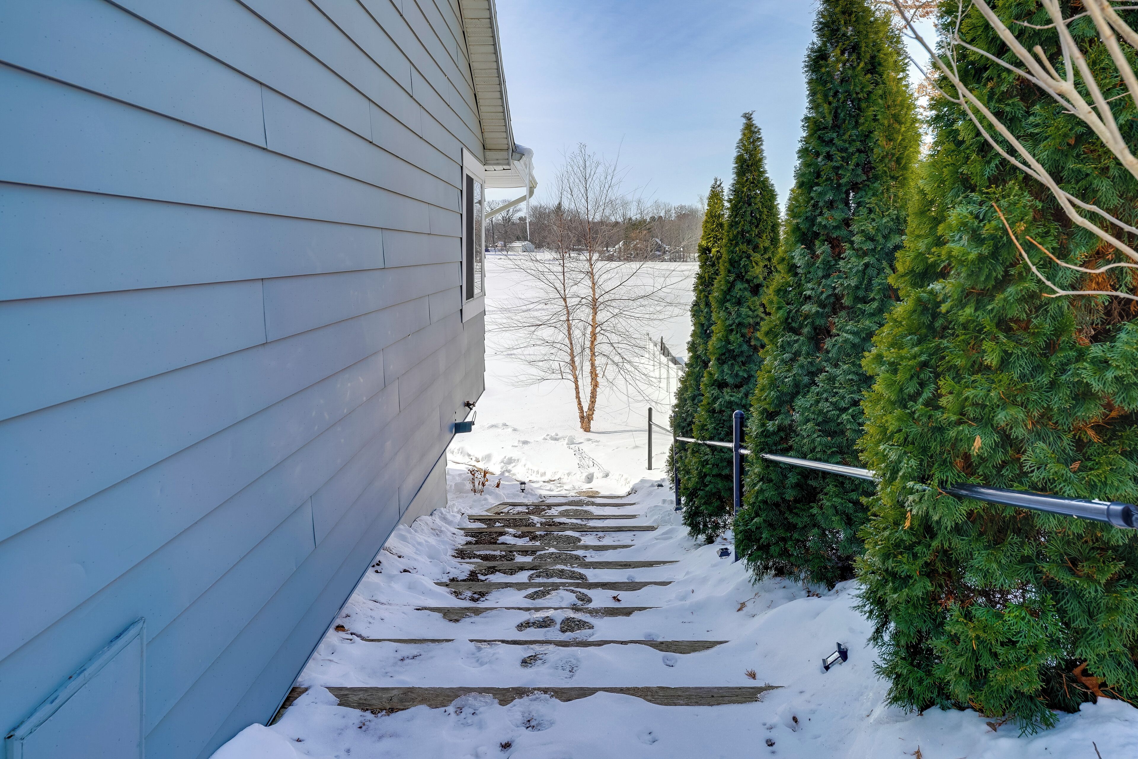 A snow-covered pathway leading to a house with a blue exterior.