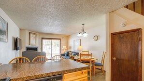 A compact kitchen with a granite countertop, wooden cabinetry, and a dishwasher. There is a dining area with a table and chairs, and a sofa in the background. - Heated Pool & Hot Tub! Winter Park Mtn Retreat (Winter Park)