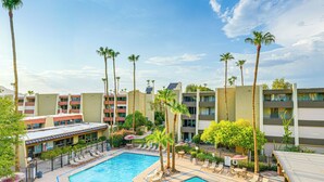 Ein Hotelpoolbereich mit rechteckigem Pool, Liegestühlen, Palmen und einem mehrstöckigen Gebäude mit Balkonen.