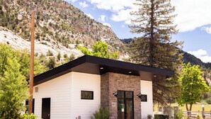 A building with a white exterior, a stone facade, and a black roof. - NEW! Unique Modern Glamping Chalet #3 (Orderville)