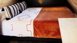 A triangular sleeping area with a bed, pillows, and a view of a landscape through a window. - NEW! Unique Modern Glamping Chalet #3 (Orderville)