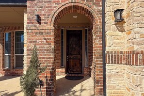 A stone building with a brick entrance, a small tree, and a door with a doormat. - Modern Home w/ Office: Near Parks, Lake & Golf! (Little Elm)