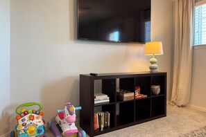 Ein Wohnzimmer mit einem an der Wand befestigten Fernseher, einem Bücherregal und einem Spielpferd.
