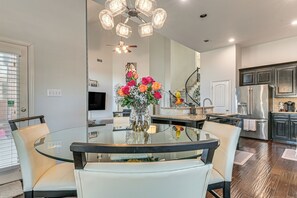 A modern kitchen with a glass dining table, white chairs, a stainless steel refrigerator, and a decorative vase with flowers. - Modern Home w/ Office: Near Parks, Lake & Golf! (Little Elm)