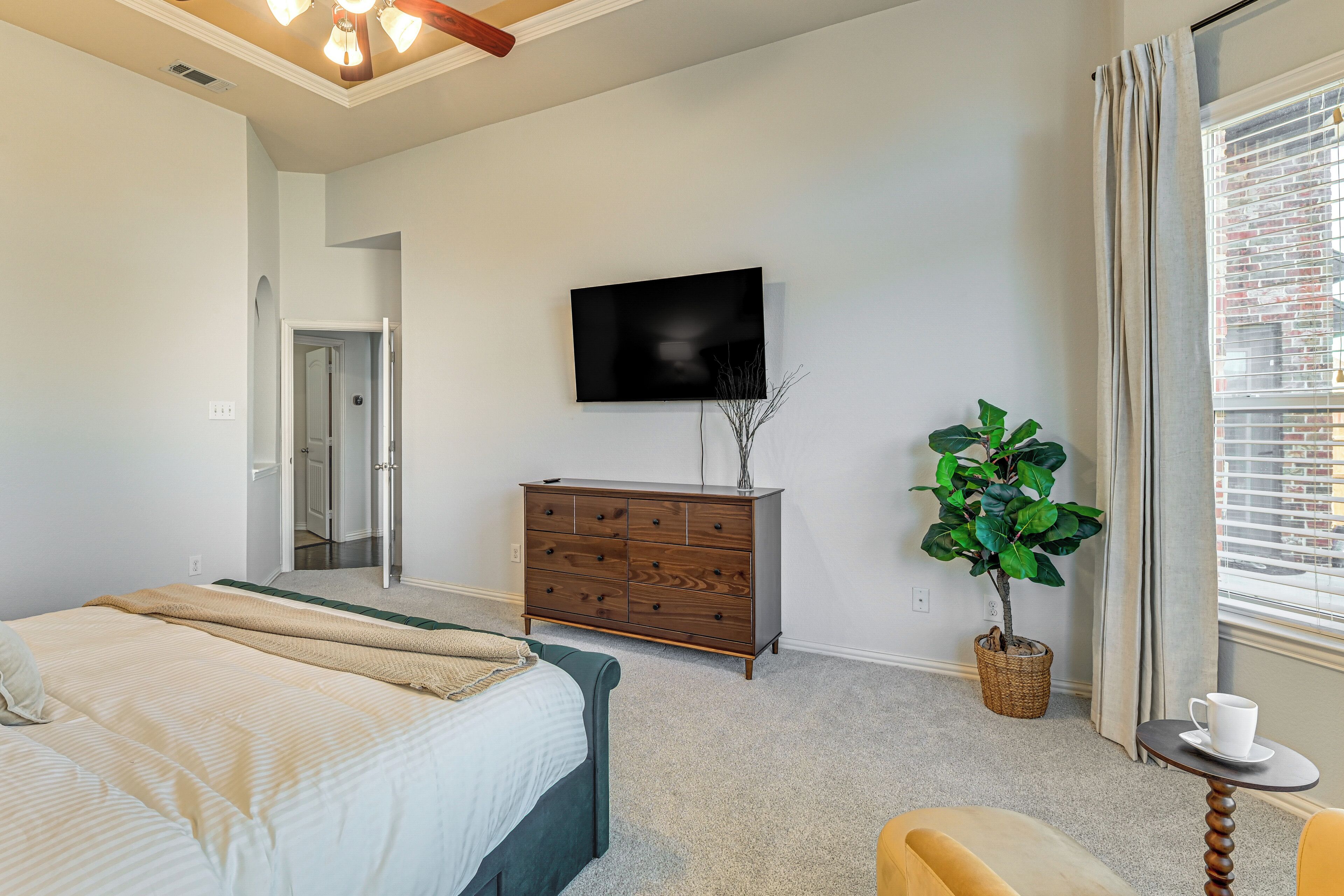 Un dormitorio con cama, cómoda, televisor, planta en maceta y ventana con cortinas.