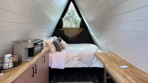 Une chambre confortable située sous les toits, avec un plafond en pente, un lit, une petite kitchenette et une fenêtre donnant sur les arbres.
