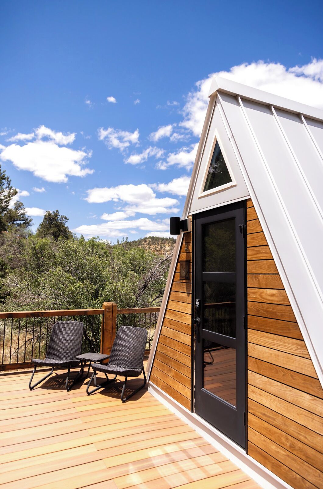 Un bâtiment moderne de forme triangulaire, doté d’une terrasse en bois et de deux fauteuils en osier.