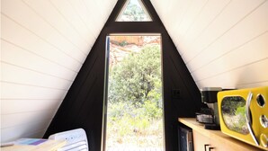Une pièce avec un plafond triangulaire, une fenêtre donnant sur un paysage rocheux, un four à micro-ondes jaune et une machine à café.