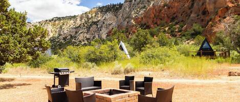 An outdoor seating area with chairs and a fire pit, surrounded by a gravel ground and a mountainous backdrop.