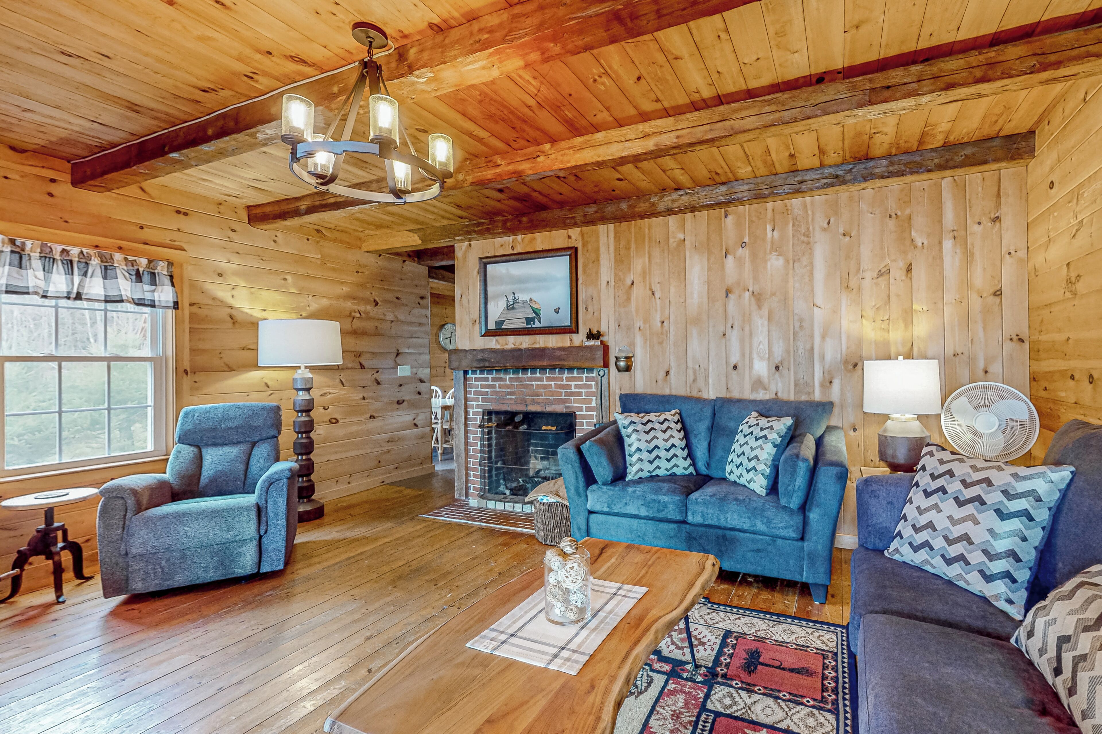 A cozy log cabin interior with a fireplace, blue sofas, and wooden flooring.