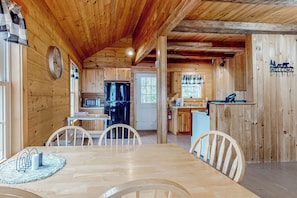 Interior de una cabaña de madera con comedor, cocina y un cartel de bienvenida.