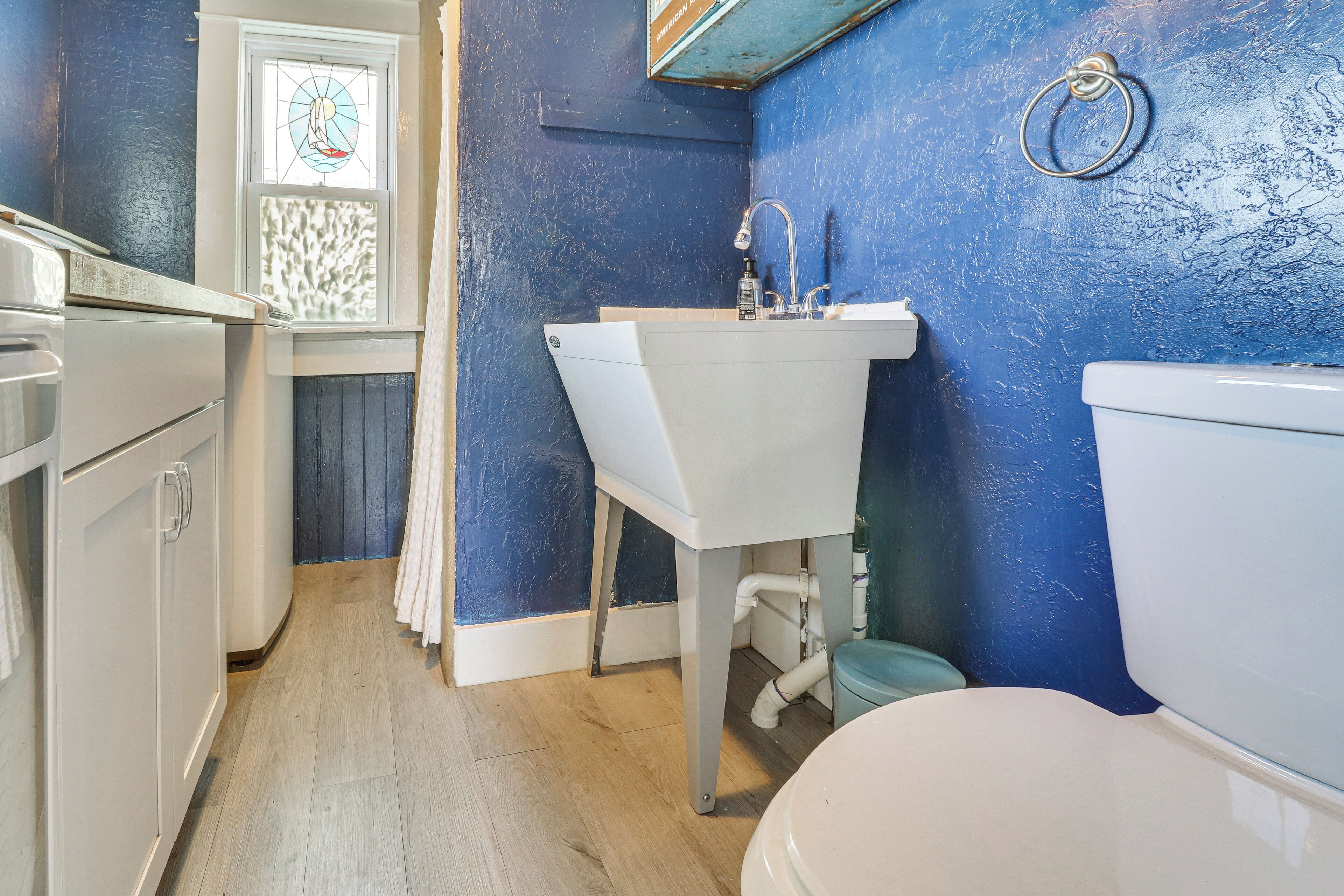 Un baño con un lavabo blanco, un inodoro y una ventana con un diseño de vitral.