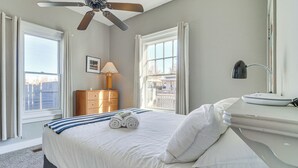 A neatly made bed with white linens and rolled towels, a bedside table with a lamp, and a view of the city through large windows. - Deck & Home Office: Walkable Albuquerque Home (Albuquerque)