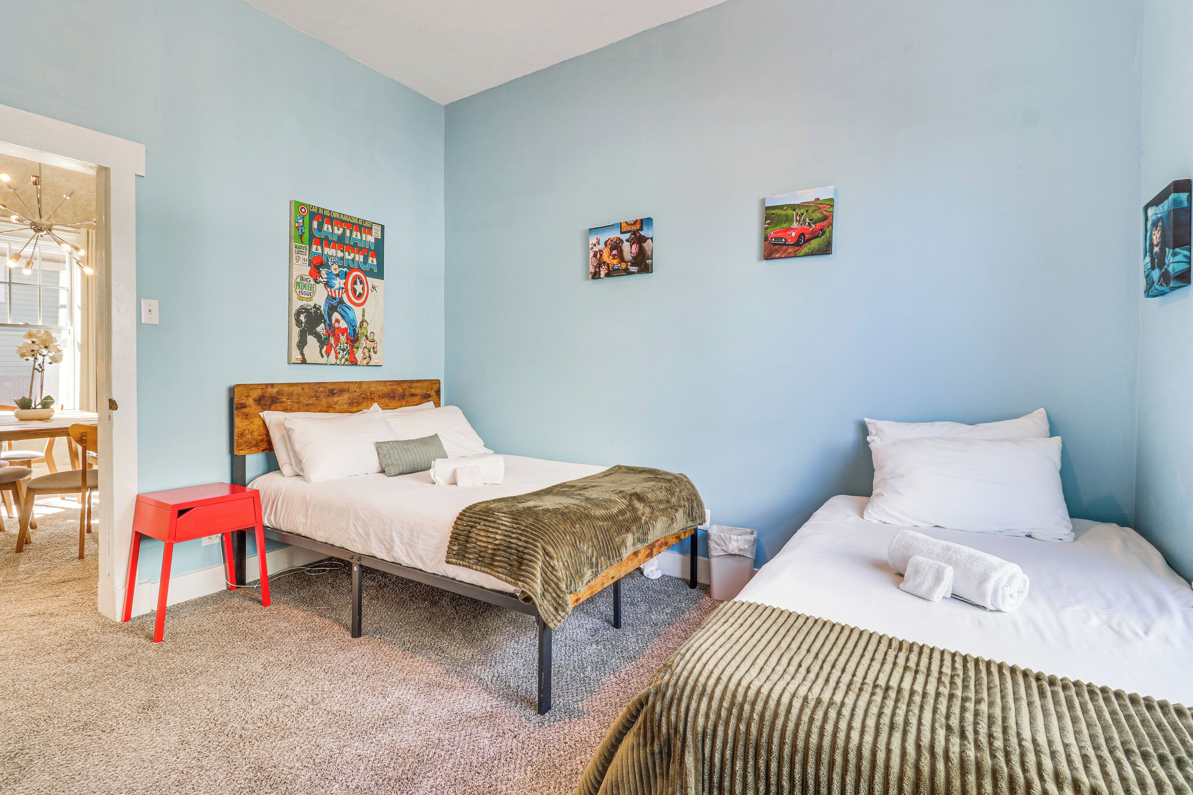 Una camera da letto con due letti, uno sgabello rosso, una testiera in legno e un poster appeso al muro.