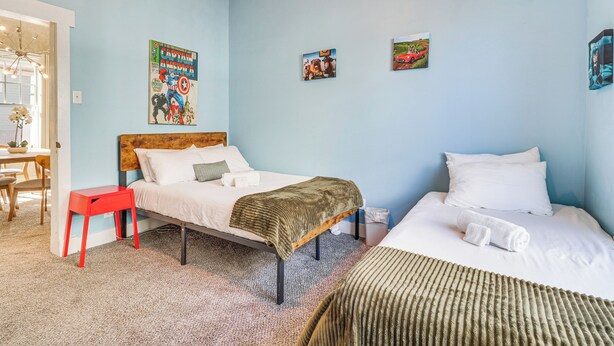 A bedroom with two beds, a red stool, a wooden headboard, and a poster on the wall.