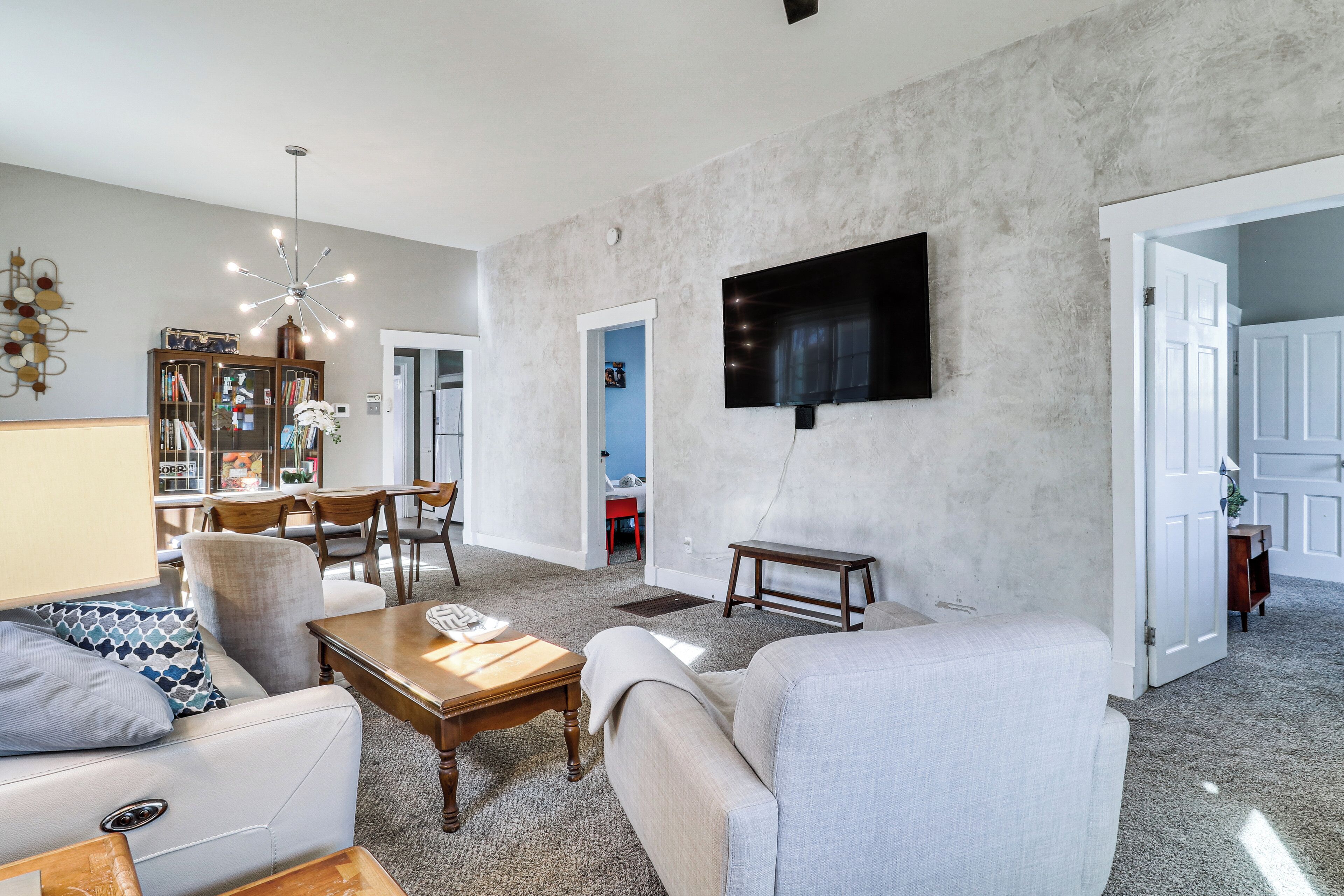 Un salon comprenant un canapé, un fauteuil et une table basse, un coin repas avec des chaises et une table, et un téléviseur fixé sur un mur à texture.