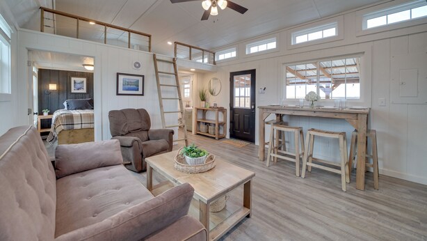A spacious living area with a high ceiling, a ceiling fan, and a large window. There is a sofa, a coffee table, and a wooden bench.