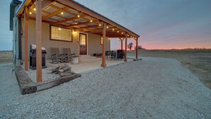A rustic cabin with a covered porch, outdoor seating, and a gravel driveway.