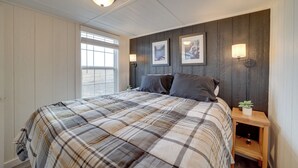 A bedroom with a plaid bedspread, a wooden nightstand with a lamp, and two framed pictures on the wall.