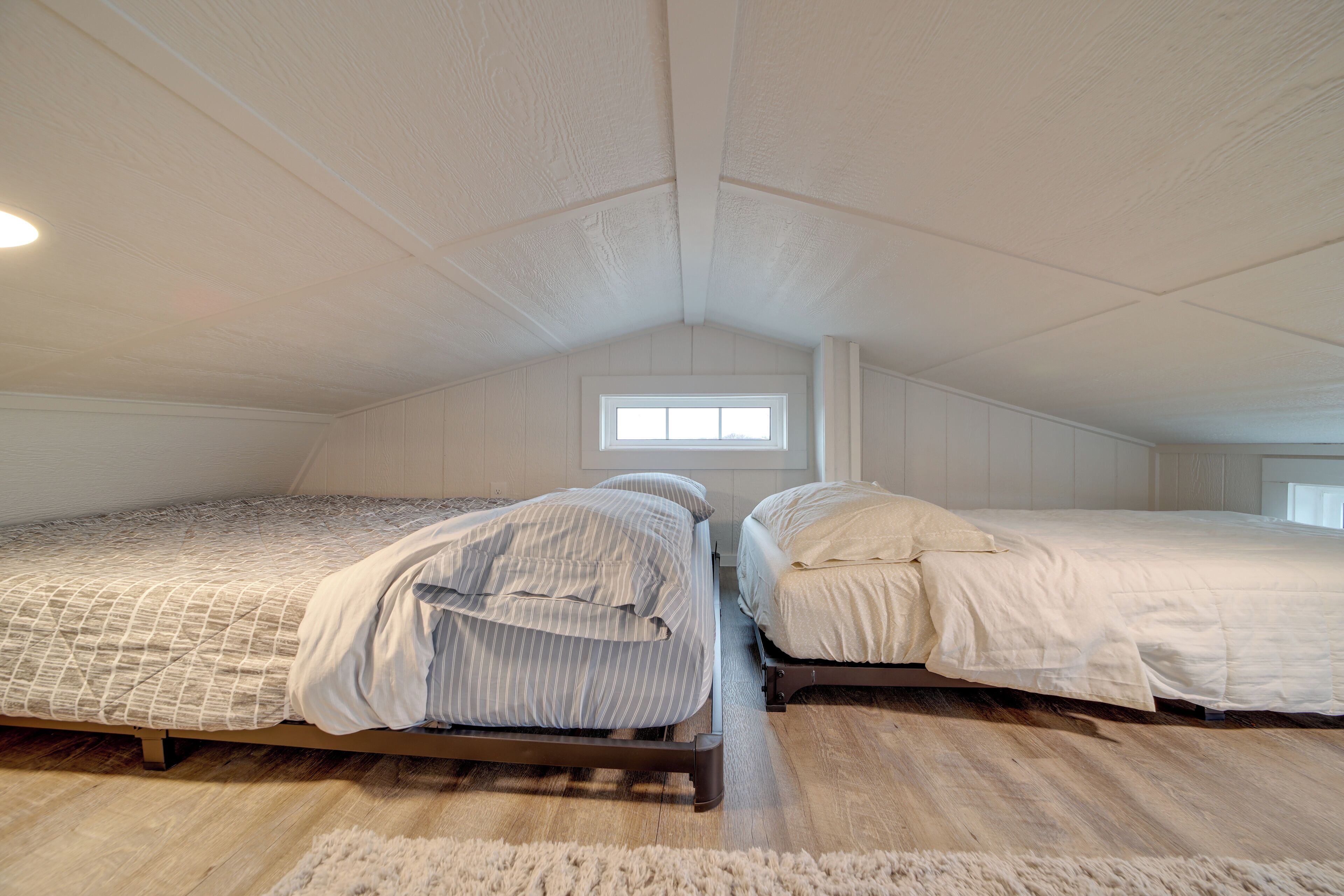 A bedroom with two beds, a window, and a wooden floor.