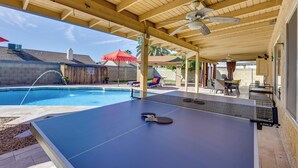 Een overdekte buitenruimte met een pingpongtafel, een zwembad en tuinmeubilair.
