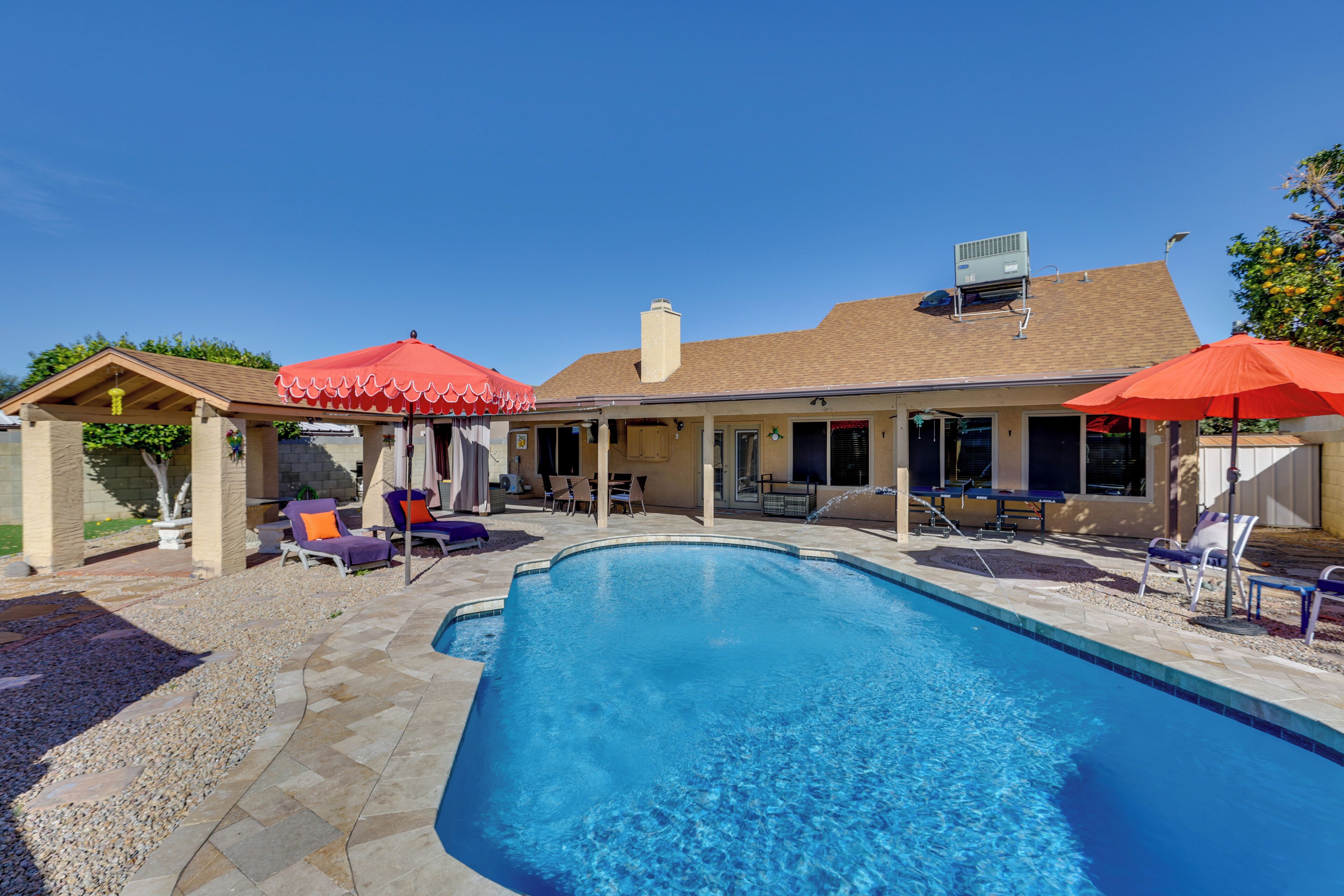 A swimming pool with lounge chairs and umbrellas, a covered patio area, and a brick exterior.
