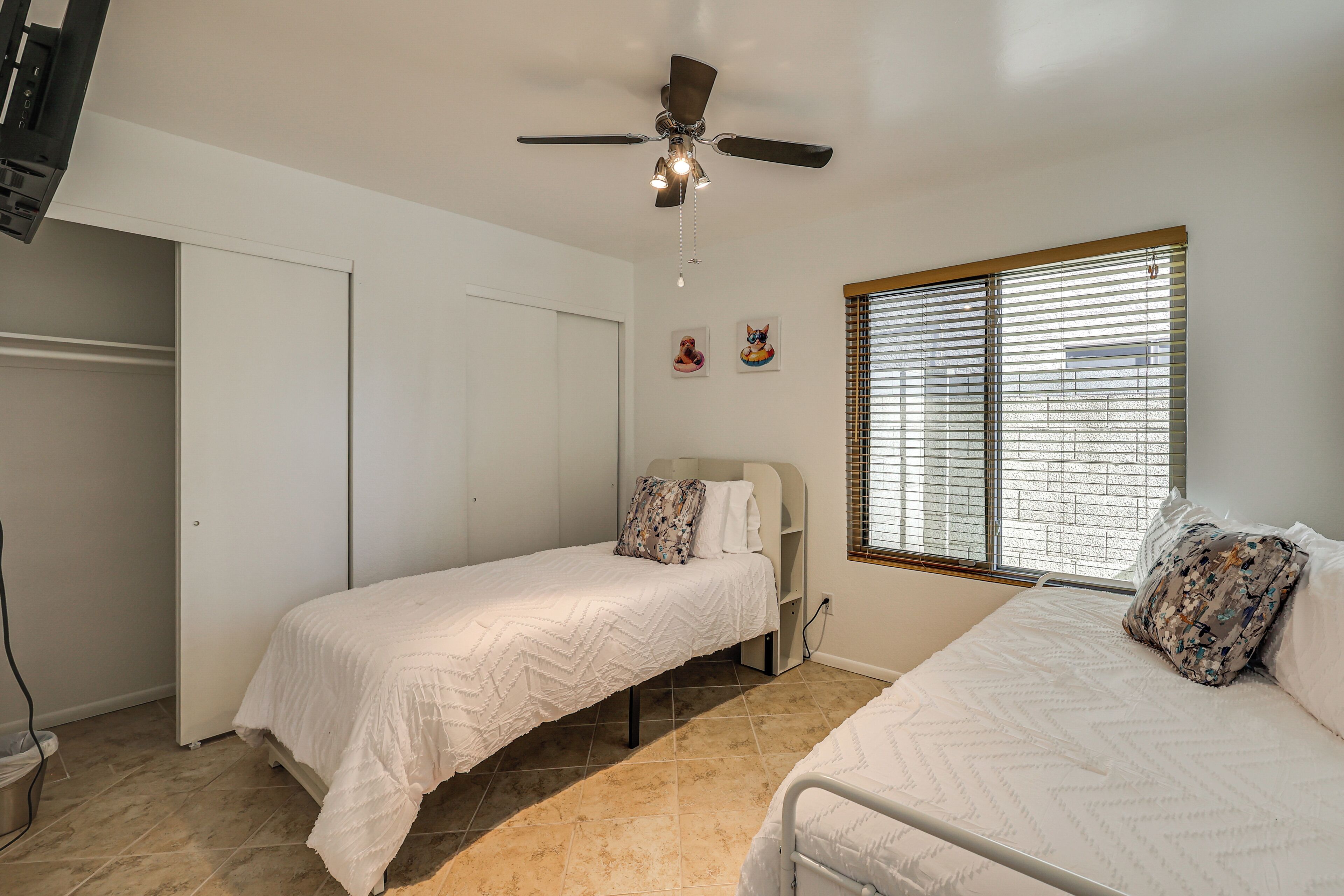 A bedroom with two beds, a ceiling fan, a window with blinds, and a white wardrobe.