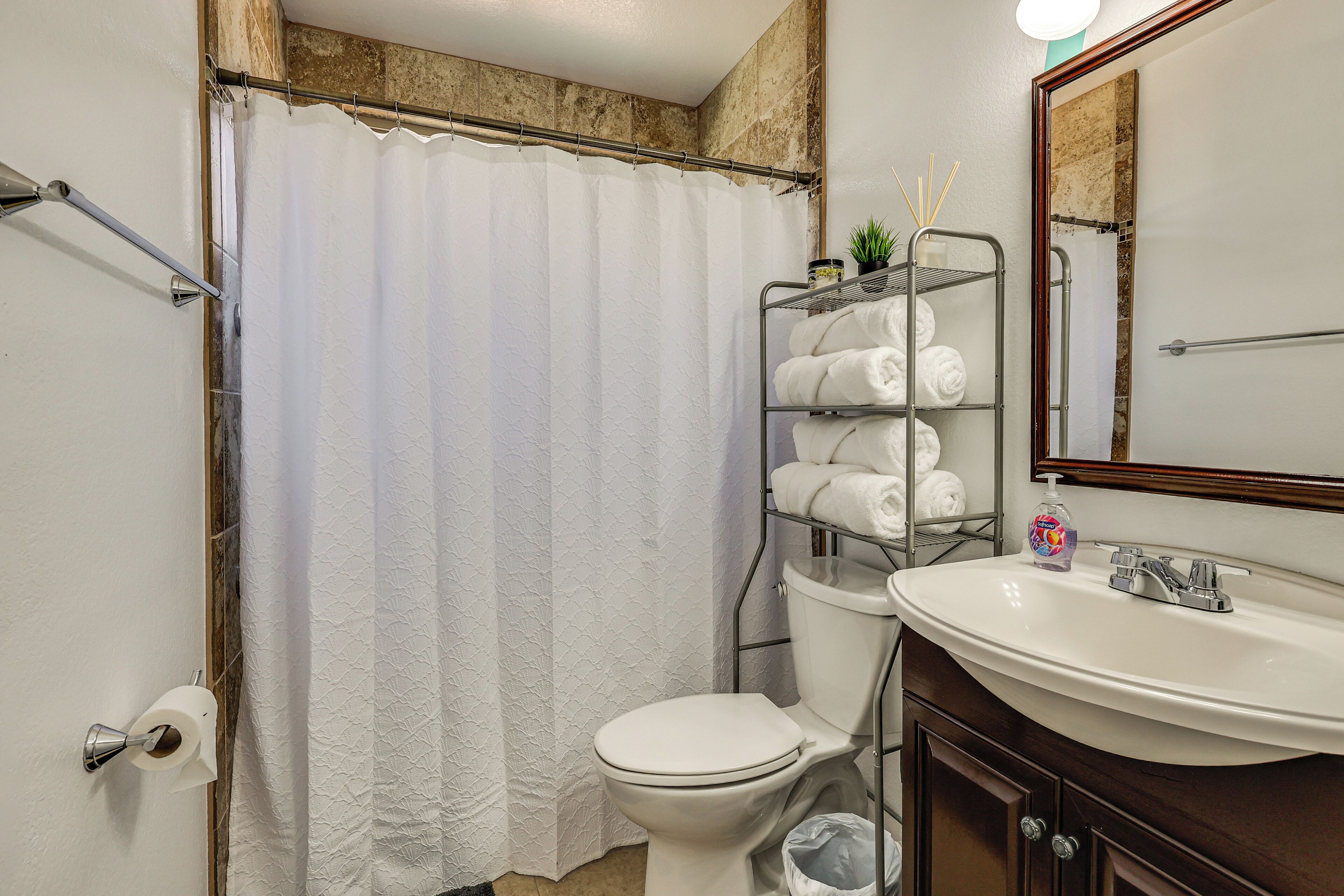 A bathroom with a white toilet, a white sink, a shower curtain, a towel rack with towels, and a mirror.