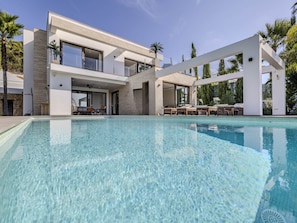 A modern two-story house with a swimming pool, outdoor seating, and a stone wall.