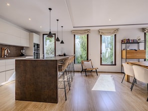 A modern kitchen with a central island, bar stools, and pendant lighting.
