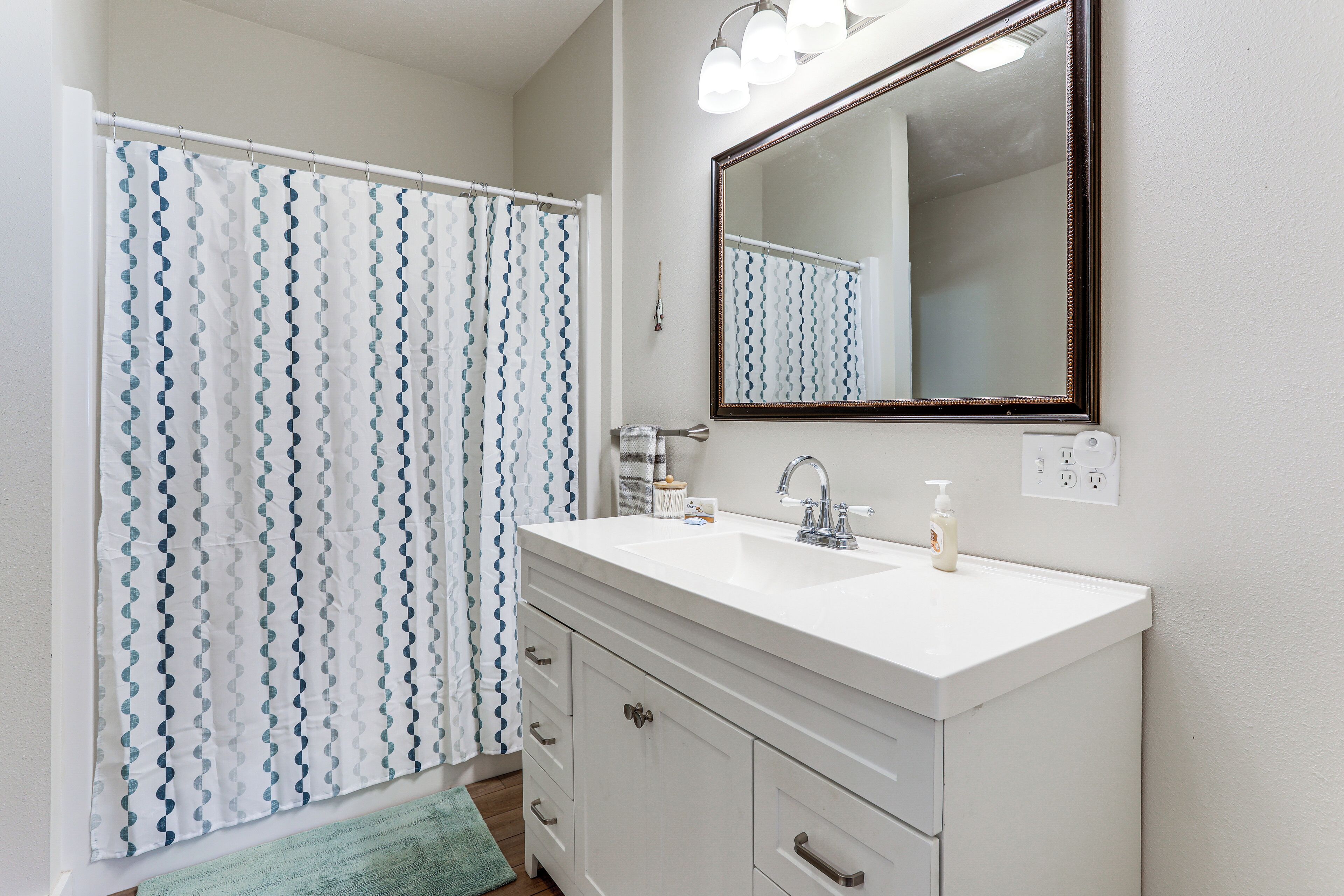 A bathroom with a white vanity, a large mirror, and a shower curtain with a blue and white pattern.