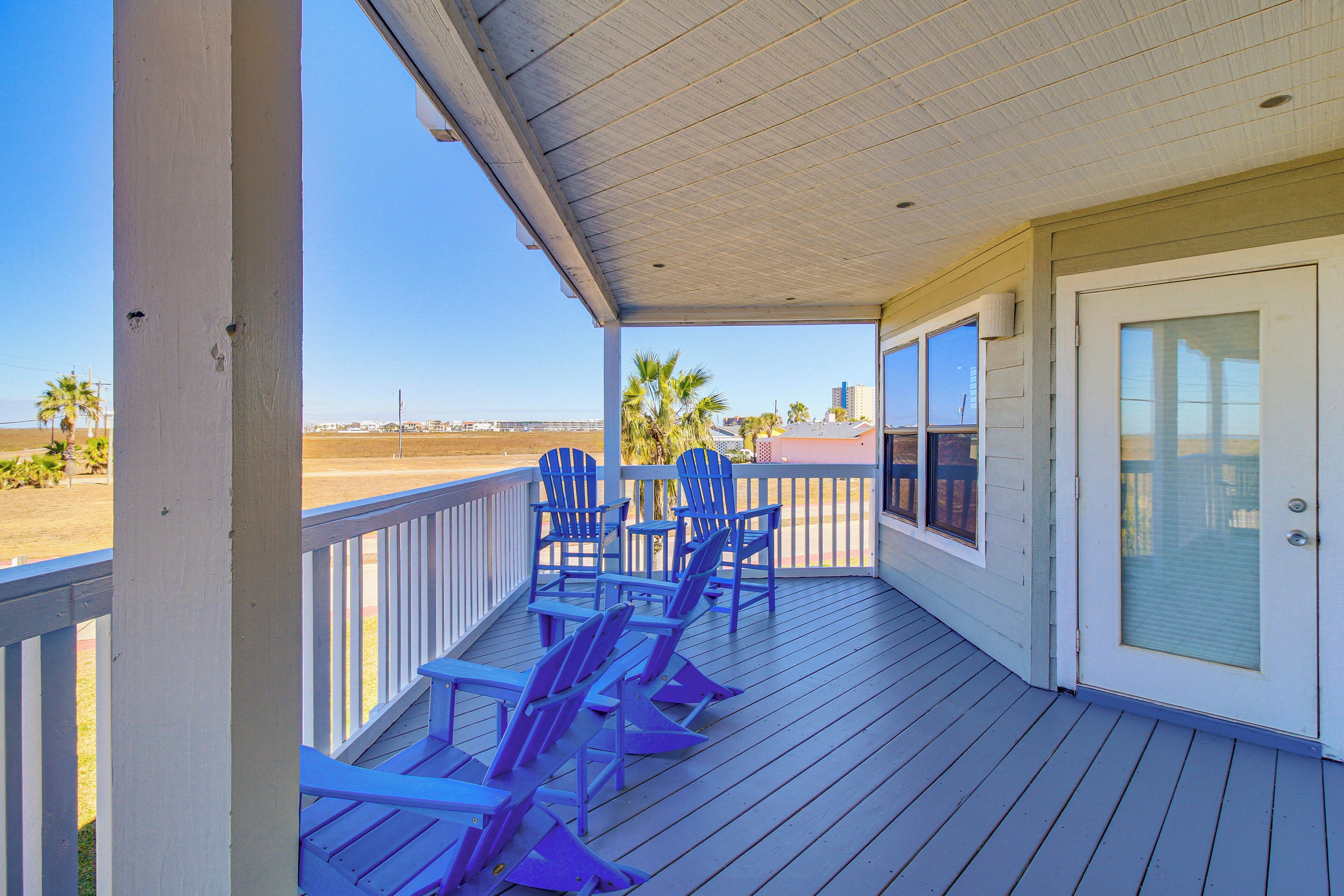 A covered porch with blue Adirondack chairs, a glass door, and a view of the beach.