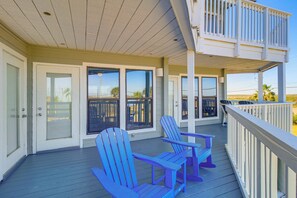 A covered porch with two blue Adirondack chairs, a white railing, and a view of the beach. - Beach Boardwalk Stay, 10-min Walk, 2-min Drive (Port Aransas)