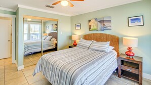 Un dormitorio con cama, ventilador de techo, mesita de noche con lámpara y espejo.