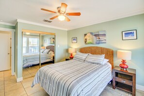 A bedroom with a bed, a ceiling fan, a nightstand with a lamp, and a mirror. - Beach Boardwalk Stay, 10-min Walk, 2-min Drive (Port Aransas)