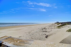 A beach with a wooden walkway leading to the shore, a sandy beach, and a distant building. - Beach Boardwalk Stay, 10-min Walk, 2-min Drive (Port Aransas)