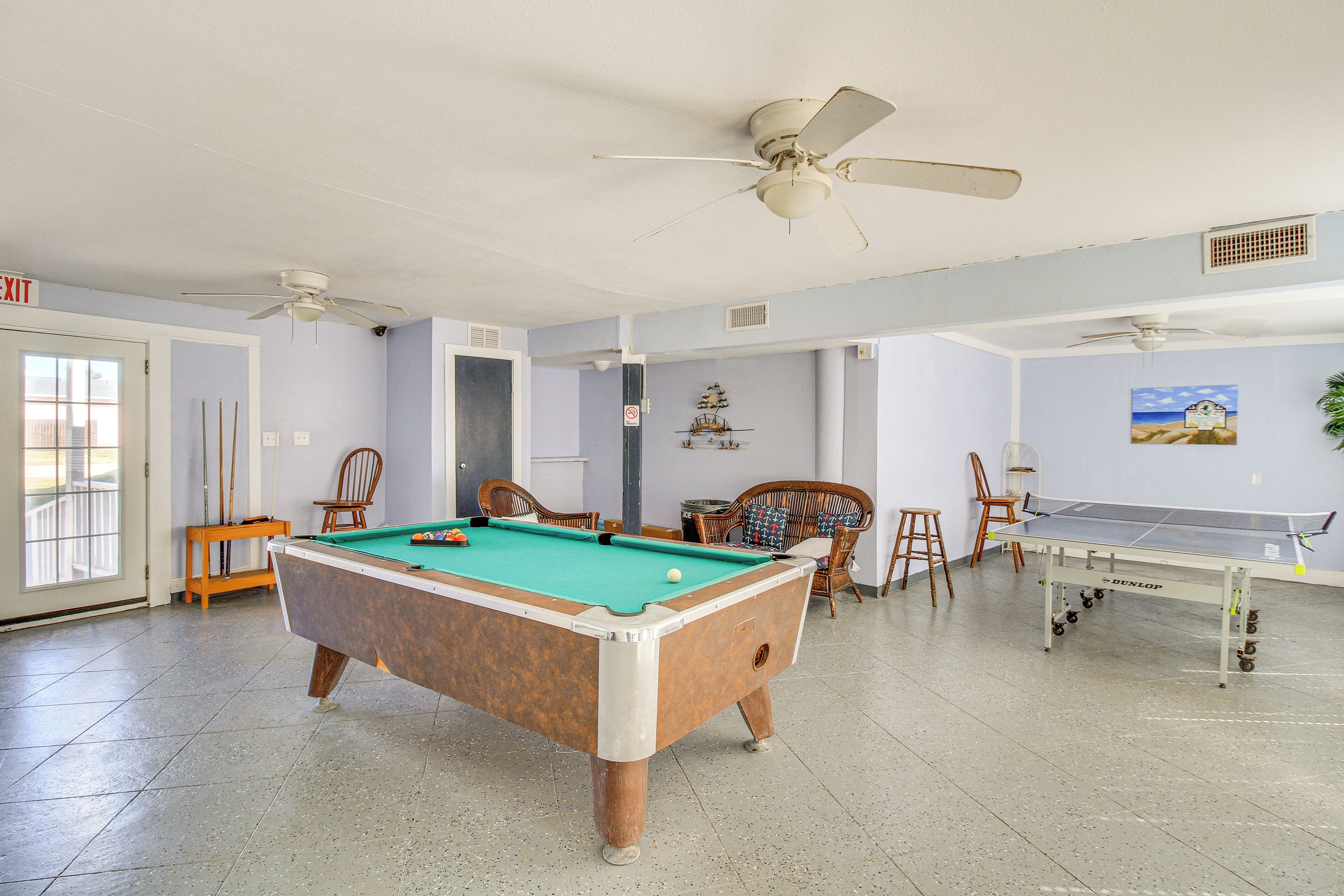 A pool table in a room with ceiling fans, a ping pong table, and a door marked "EXIT".