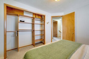 A bedroom with a bed, a green knitted blanket, a wooden wardrobe with shelves, and a door leading to another room.